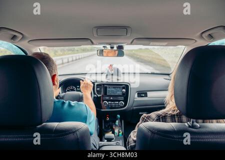 Fahrer, der das Lenkrad in einem modernen Fahrzeug hält, während der Beifahrer auf dem Vordersitz sitzt, Roadtrip, Armaturenbrett im Inneren, Navigationsbildschirm, Rückspiegel Stockfoto
