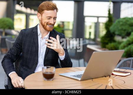 Junger Geschäftsmann in Anzug bei Videogesprächen im Café im Freien Stockfoto