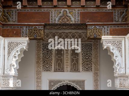 Geschnitzter Stuck und Zedernholzfries mit arabischer Kalligraphie und kleinen Bogenfenstern an der Hofwand von Ben Youssef Madrasa (Medersa Ben Youssef) Stockfoto