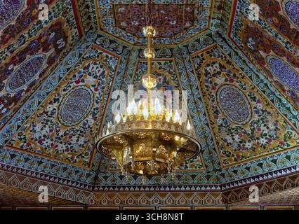 Reich verzierter Empfangsraum mit gemalter Zedernholzdecke, Kronleuchter und gekacheltem Kamin im Bahia Palace (Palais Bahia), Marrakesch, Marokko. Stockfoto