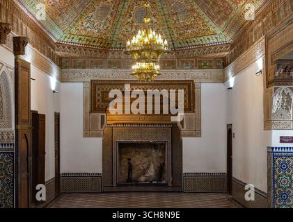 Reich verzierter Empfangsraum mit gemalter Zedernholzdecke, Kronleuchter und gekacheltem Kamin im Bahia Palace (Palais Bahia), Marrakesch, Marokko. Stockfoto