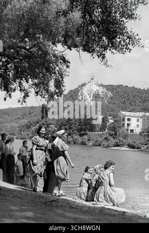 Ein einzigartiges historisches Foto, das eine Gruppe von Pilgern, darunter eine Frau in klösterlicher Kleidung (eine Nonne), am Ufer des Sewerski Donets in Swiatohirsk während der Sowjetzeit (etwa 1960er-70er Jahre) feststellt. Der Hintergrund zeigt die ikonische Landschaft mit dem kommunistischen Denkmal für Artem auf dem Hügel über dem Heiligen Gebirge Lavra, das damals ein Sanatorium war. Der Schuss ist ein seltenes Zeugnis für die Erhaltung des spirituellen Lebens und Glaubens in einer Zeit des staatlichen Atheismus und zeigt die tiefen spirituellen Wurzeln des Donbass Stockfoto