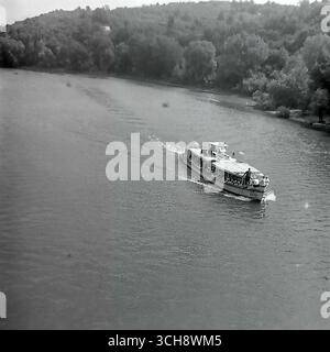Eine dynamische Szene des Flusslebens am Sewerski Donets in Swiatohirsk in den 1970er-80er Jahren Der Rahmen zeigt verschiedene Schiffe, von Freizeitbooten und Flussbahnen voller Touristen bis hin zu schnellen Motorbooten, die sich vor der berühmten Landschaft der Heiligen Berge Lavra und Kreidehügel befinden. Das Foto vermittelt die Atmosphäre eines beliebten sowjetischen Resorts und ist ein anschauliches Zeugnis für den entwickelten Wassertourismus. Es ist ein nostalgisches Bild eines aktiven Sommerurlaubs und ein Symbol für das friedliche, unbeschwerte Leben im Donbass vor dem Krieg Stockfoto