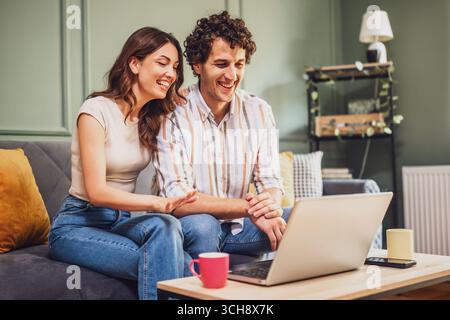 Ein Ehemann und eine Frau, die sich auf ihrem Laptop fröhlich unterhalten, Lachen teilen und bequem über das Internet in Verbindung bleiben Stockfoto
