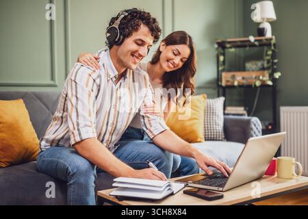 Ein Mann und eine Frau sitzen zu Hause zusammen und überprüfen ihre Einkaufsliste, während sie einen Laptop benutzen. Ihre Zusammenarbeit unterstreicht den organisierten Ansatz Stockfoto