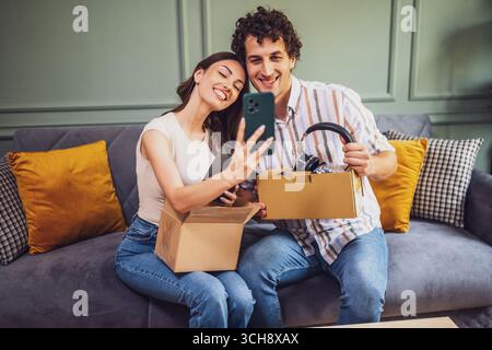 Ein erwachsenes Paar packt ihre Pakete aus, die an die Heimatadresse geliefert werden. Sie machen Selfie mit neuen Gegenständen. Stockfoto
