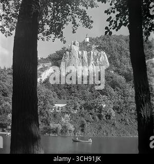 Eine klassische Landschaft von Sviatohirsk aus den 1970er-80er Jahren mit der berühmten Nikolaikirche auf einer Kreidefelse. Die Aussicht wird geschickt von zwei mächtigen Bäumen eingerahmt, was eine tiefe und künstlerische Komposition schafft. Ein Boot mit Urlaubern ist auf dem Seversky Donets River zu sehen, und Gerüste können auf dem Gipfel des Berges gesehen werden. Diese Aufnahme ist die Quintessenz der Schönheit von „Donets Schweiz“ und vermittelt eine Atmosphäre der Harmonie, Ruhe und eines friedlichen, besinnlichen Lebens vor dem Krieg Stockfoto