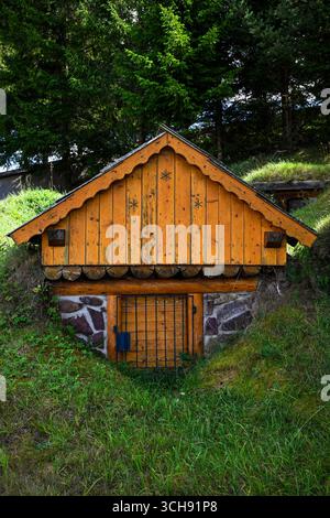 Holzkeller, der in einen Hügel eingebettet ist und von Wald umgeben ist, zeigt traditionelle Techniken zur Konservierung von Lebensmitteln. Stockfoto