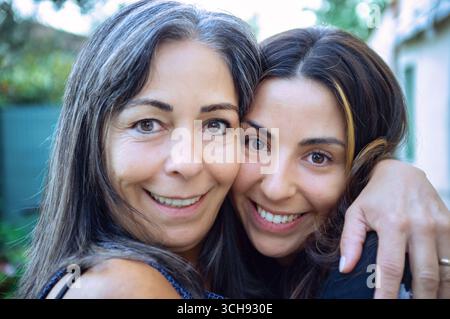 Nahporträt einer lächelnden Mutter und einer erwachsenen Tochter, die sich umarmen und in die Kamera schauen. Familienbindung, Liebe und Glück. Tageslicht, Ou Stockfoto