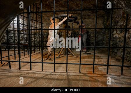 Gefängniswärter foltert Frau mit mittelalterlichem Foltergerät in dunklem Kerker. Stockfoto