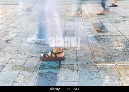 Leute, die tagsüber auf dem Bürgersteig laufen. Bewegungsverschwommene Beine von Fußgängern. Stockfoto