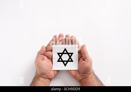 Männliche Hände mit einer weißen Note, auf der ein Stern von David gezeichnet ist, der jüdische Religion, Kultur und Erbe auf weißem Hintergrund repräsentiert Stockfoto