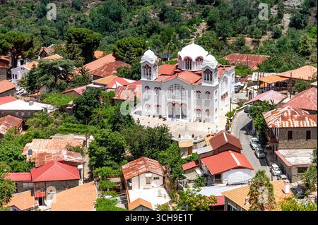 Blick aus der Vogelperspektive auf das Dorf Pedoulas in den Troodos-Bergen, Zypern, mit Blick auf die markante weiße Kirche inmitten traditioneller Häuser mit rot gekachelten Zimmern Stockfoto