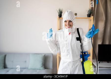 Positiv lächelnde weibliche Exterminatorin vom Schädlingsbekämpfungsdienst, die im Haus mit Sprühflasche arbeitet und gute Emotionen zu Hause hat. Kopierbereich Stockfoto