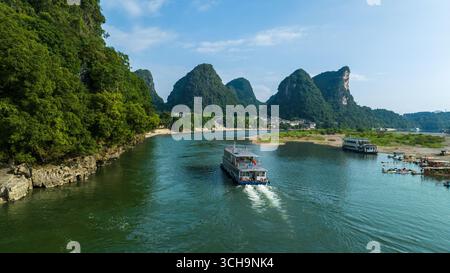 Aus der Vogelperspektive eines Bootes, das durch den jadegrünen Li River fährt, umgeben von den majestätischen, grünen Karstbergen unter einem ruhigen Himmel, Yangshuo, China. Stockfoto
