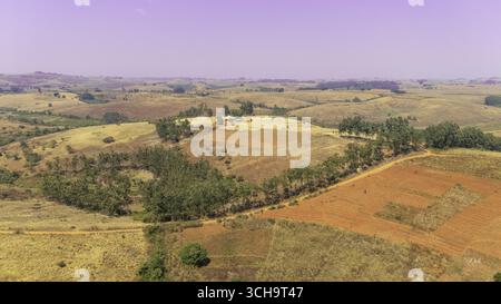 Aus der Vogelperspektive auf sanfte Hügel in Erdbraun und Grün, zusammengenäht von einer unbefestigten Straße unter einem trüben Himmel, Njawai, Taraba, Nigeria. Stockfoto