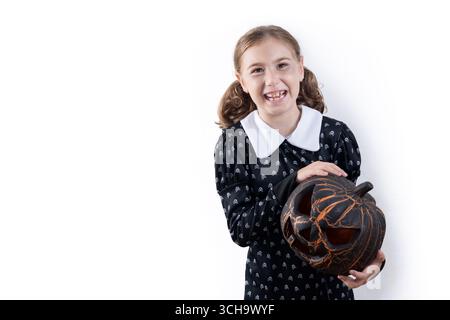 Lächelndes Mädchen im Halloween-Kostüm, das einen Halloween-Kürbis hält Stockfoto