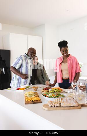 Familie genießt Zweisamkeit und Lachen bei der Zubereitung von Mahlzeiten in der modernen Küche. Kochen, Lifestyle, Binden, Vorbereitung, Teamarbeit, fröhlich Stockfoto