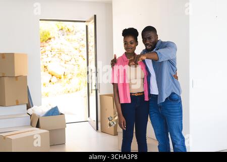 Afroamerikanisches Paar plant ein neues Zuhause, umgeben von Umzugskartons, und fühlt sich aufgeregt. Aufregung, Umzug, gemütlich, auspacken, Teamwork Stockfoto