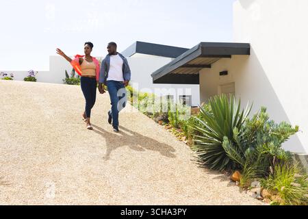 Afroamerikanisches Paar, das an sonnigen Tagen draußen spaziert, Gespräche genießt und Hände hält. Romantik, Beziehung, Glück, Sonnenschein, Bindung Stockfoto