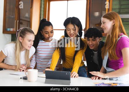 Verschiedene Teenager versammelten sich in der Küche um ein Tablet und sahen sich zu Hause gemeinsam Videos an. Technologie, Digital, Bindung, Freundschaft, Unterhaltung Stockfoto