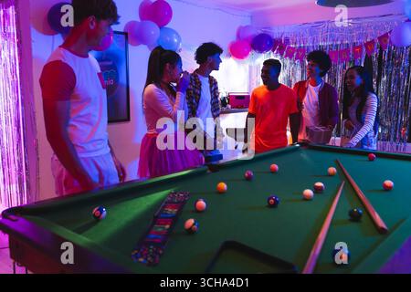 Abwechslungsreiche Teenager genießen lebhafte Geburtstagsparty am Billardtisch mit Dekoration, zu Hause. Feierlich, festlich, Billard, gesellig, fröhlich, le Stockfoto