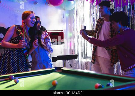 Verschiedene Teenager-Freunde posieren für Smartphone-Foto auf Party, feiern in der Nähe des Billardtisches, zu Hause. Teenager vielfältige Freunde, Feier, Freundschaft, Stockfoto