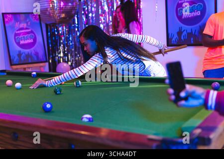 Teenager spielen Billard auf der Party, fokussieren sich auf den Schuss, während Freunde in der Nähe feiern, zu Hause. Billard, Feier, Teenager-Freunde, Freundschaft, Stockfoto
