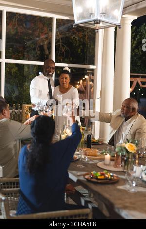 Bei der Hochzeit toast Seniorenpaar mit Freunden bei einem eleganten Abendessen im Freien. Ältere Menschen, Freundschaft, Essen, draußen, Party, sammeln Stockfoto