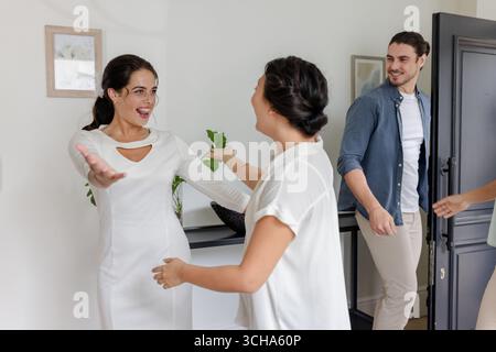 Braut in weißem Kleid begrüßt Freunde zu Hause während einer kleinen zwanglosen Hochzeitsfeier, zu Hause. Freundschaft, Glück, Kleid, fröhlich, festlich Stockfoto