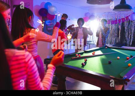 Teenager feiern Geburtstag mit Glitzern am Billardtisch im festlichen Raum. Feier, Teenager, Party, Billard, Freunde, begeistert Stockfoto