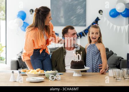 Wir feiern Geburtstag, fröhliche Familie genießt Kuchen und Lachen zu Hause. Feier, Glück, Zweisamkeit, Party, Wohnzimmer Stockfoto