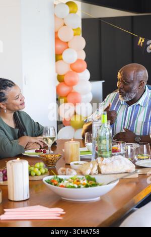 Freunde genießen Gespräche und Wein am festlichen Dinner-Tisch mit Ballons. Feiern, Treffen, Essen, Zweisamkeit, Freundschaft, Party Stockfoto
