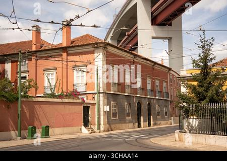 Blick auf die Straße in Lissabons Alcântara, wo die Brücke 25 de Abril in starkem Kontrast zu den charmanten alten Gebäuden steht und die Gegend geprägt hat. Stockfoto