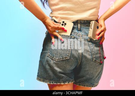 Woman in denim shorts holding smartphone and retro cassette player Stockfoto