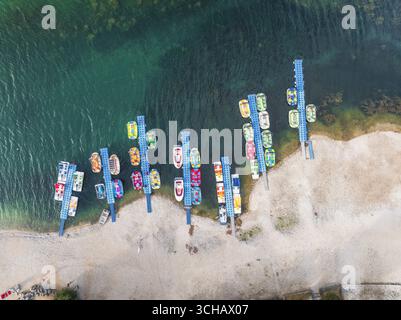 Aus der Vogelperspektive auf Tretboote, die am Ufer des Sees anlegen, ein lebhafter Kontrast zum türkisfarbenen Wasser, der eine malerische Szene schafft, Scanno, Abruzzen, Italien. Stockfoto