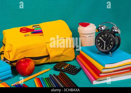 Gelber Rucksack, Bücher, Wecker und Schulutensilien bereit für den Schulbesuch Stockfoto