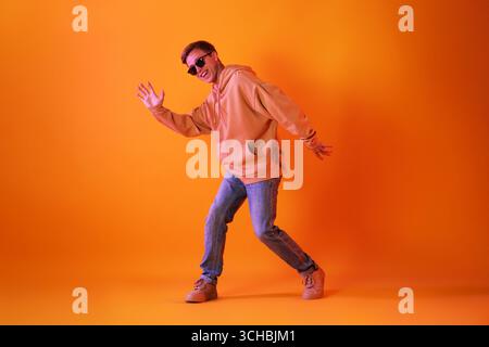 Lächelnder Mann mit Sonnenbrille, der in Neonlichtern vor orangem Hintergrund tanzt Stockfoto