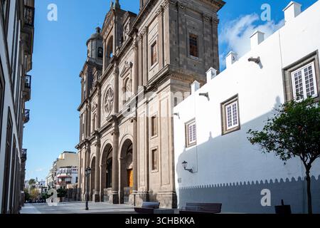 Eine große Kirche mit einer weißen Fassade und einem blauen Himmel im Hintergrund. Die Kirche ist von einer Straße umgeben, in der Menschen laufen und auf Bänken sitzen Stockfoto