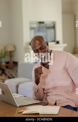 Der Afroamerikaner, der zu Hause ein Notebook benutzt, lächelt fröhlich. Leistung, Home Office, Technologie, Glück, Sieg, Fernsteuerung Stockfoto