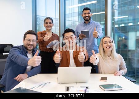 Multiethnische Geschäftsleute, die ihre Zufriedenheit mit erfolgreicher Teamarbeit zum Ausdruck bringen, in einem modernen Büro die Daumen nach oben geben, positive Ergebnisse und Co feiern Stockfoto