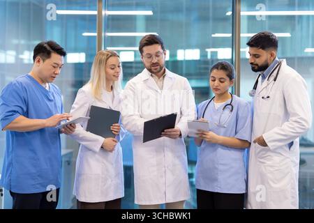 Ärzte und Krankenschwestern, die Krankenakten untersuchen und den Behandlungsplan eines Patienten in einem modernen Krankenhaus diskutieren, arbeiten zusammen, um eine effektive Arbeit zu gewährleisten Stockfoto