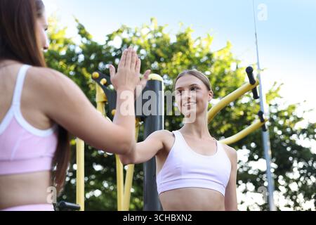 Junge Frau mit professionellem Personal Trainer, die High 5 in Outdoor Gym, selektiv fokussiert Stockfoto