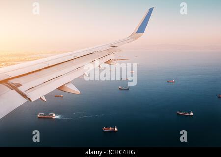 Flugzeugflügel gleitet über das Meer, enthüllt zahlreiche Frachtschiffe, die bei Sonnenuntergang in der Nähe der Küste segeln, und schafft eine ruhige Szene in Istanbul Stockfoto