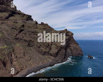 Aus der Vogelperspektive der zerklüfteten Vulkanküste Teneriffas, Spanien. Scharfe, dunkle Felsformationen unterstreichen das leuchtend blaue Wasser des Atlantischen Ozeans Stockfoto
