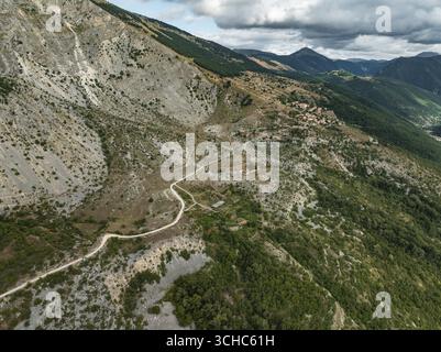 Aus der Vogelperspektive schlängelt sich eine gewundene Feldstraße durch die zerklüftete, sonnenverwöhnte Landschaft in der Nähe von Frattura Vecchia, im Kontrast zu den dramatischen, felsigen Berglandschaften, Frattura Vecchia, Abruzzen, Italien. Stockfoto