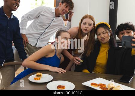 Verschiedene Teenager machen Selfie auf Partys, genießen Snacks und haben Spaß zu Hause. Feier, Freundschaft, vielfältige Teenager, Gruppe, Lebensstil Stockfoto