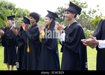 Absolventen in Mützen und Gewändern feiern Erfolge im Freien, klatschen zusammen. Abschluss, Feier, Erfolg, Bildung, Zeremonie, acad Stockfoto