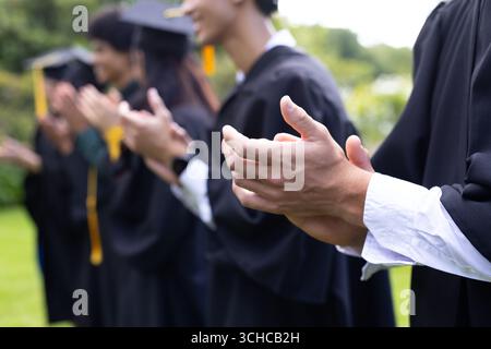 Absolventen klatschen im Freien, tragen Mützen und Kleider. Abschluss, Leistung, Zeremonie, Ausbildung, Diplom, fröhlich Stockfoto