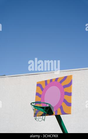 Farbenfroher Basketballkorb mit künstlichem Sonnendesign vor klarem blauem Himmel und weißer Wand Stockfoto